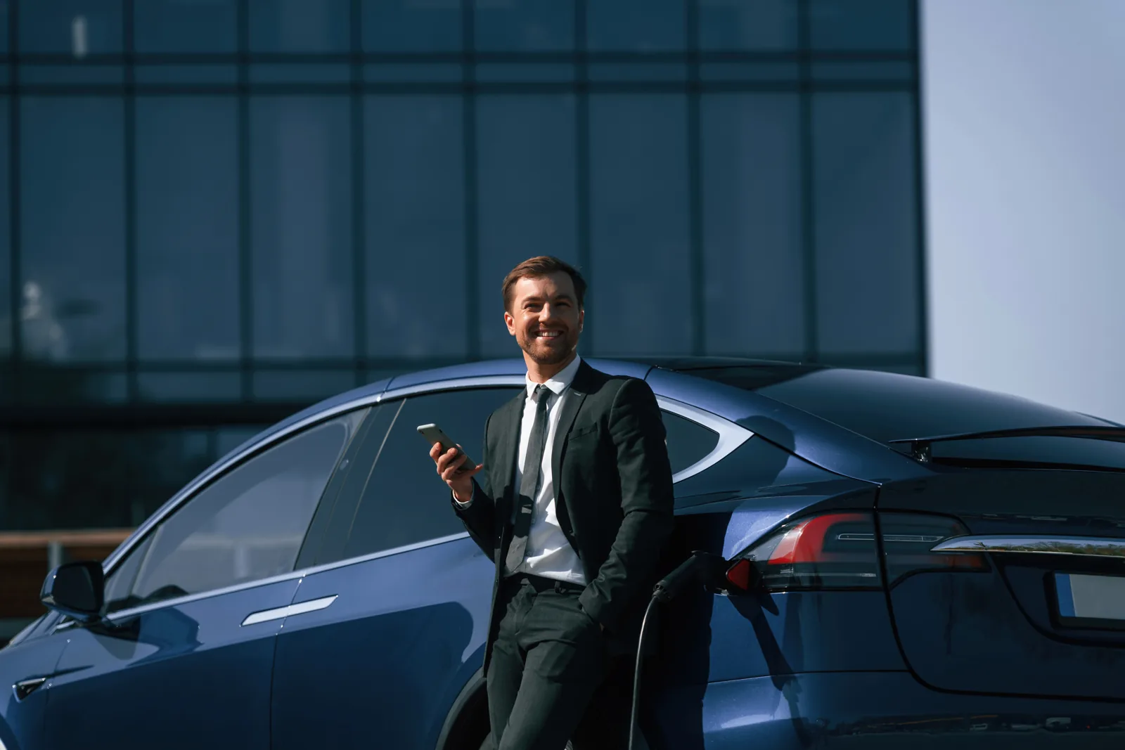 Professional checking a phone beside a blue Tesla